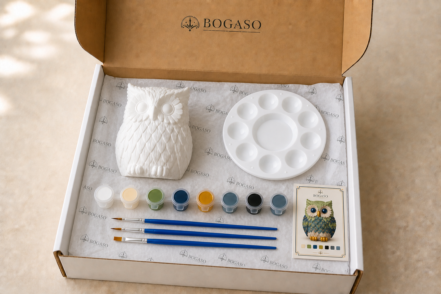 Open Bogaso box with one unpainted owl, acrylic paints, brushes, palette and color guide